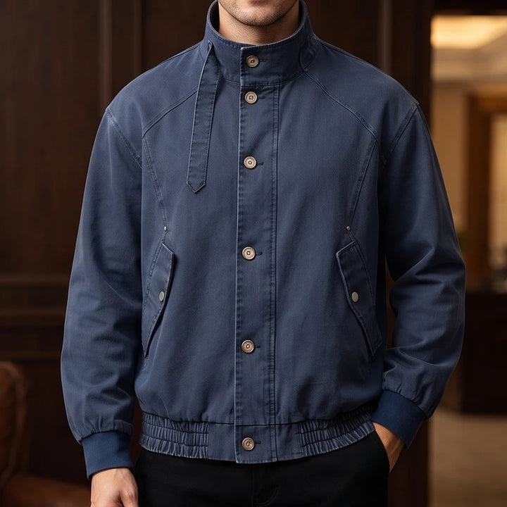Man wearing a dark blue bomber jacket with a stand-up collar, button front, flapped pockets, and ribbed cuffs.