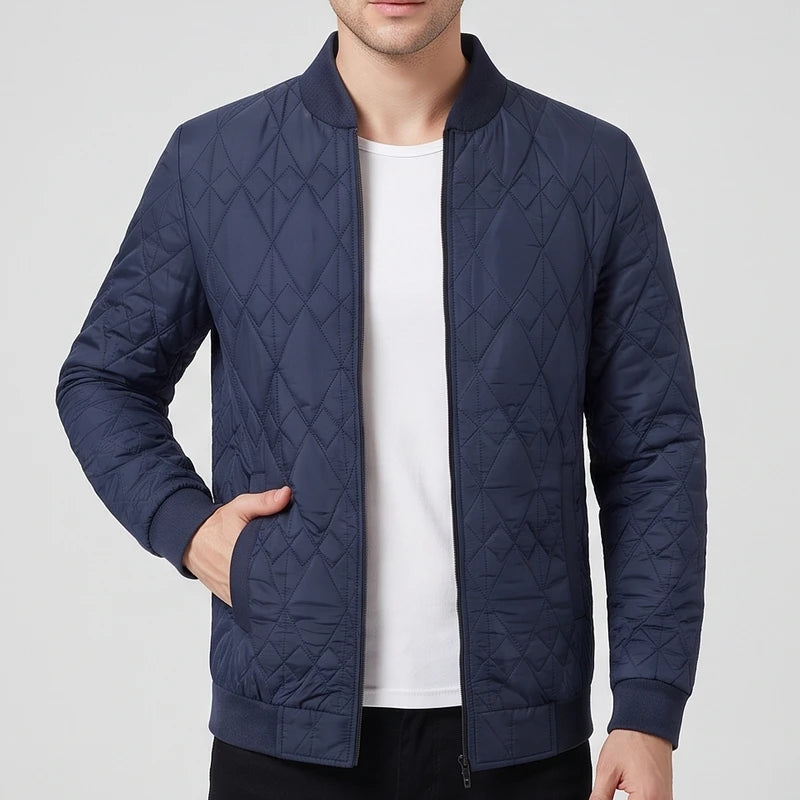 Man wearing a navy blue quilted bomber jacket with diamond pattern, ribbed collar, and cuffs, hand in pocket.