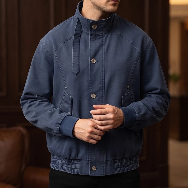 Man wearing a dark blue bomber jacket with a standing collar, buttons down the front, and ribbed cuffs and hem.
