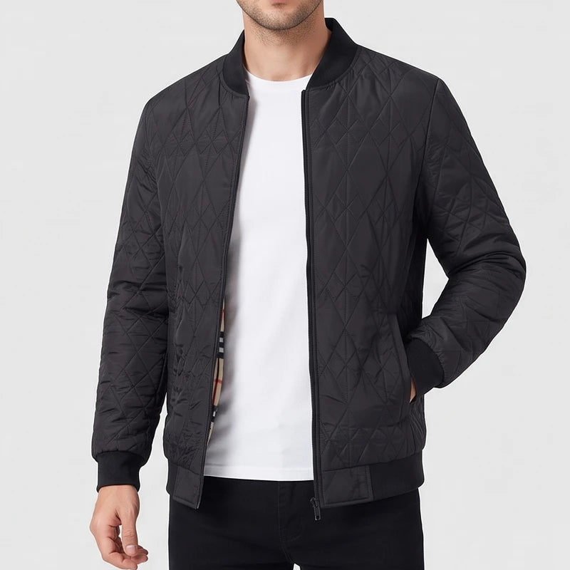 Man wearing an open black quilted bomber jacket with a ribbed collar, cuffs, and hem, standing with a hand in his pocket.