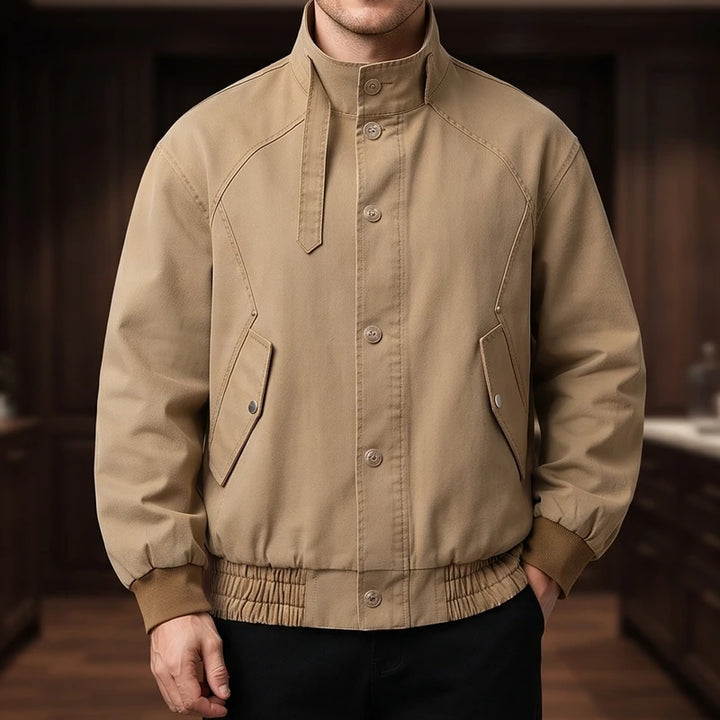 Man wearing a tan cotton bomber jacket with a stand collar, button placket, two flap pockets, and ribbed cuffs.