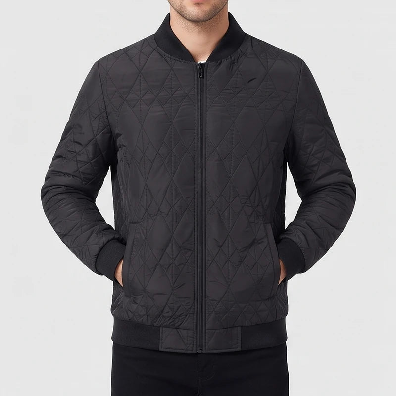 Man wearing a black quilted bomber jacket with a front zipper, ribbed collar, and his hands in the pockets.