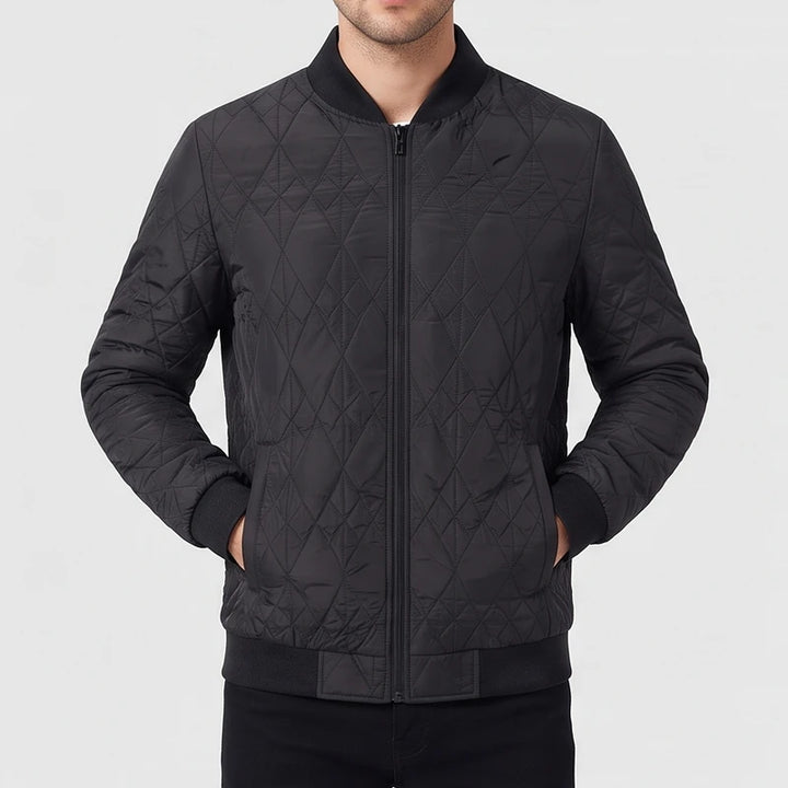 Man wearing a black quilted bomber jacket with a front zipper, ribbed collar, and his hands in the pockets.