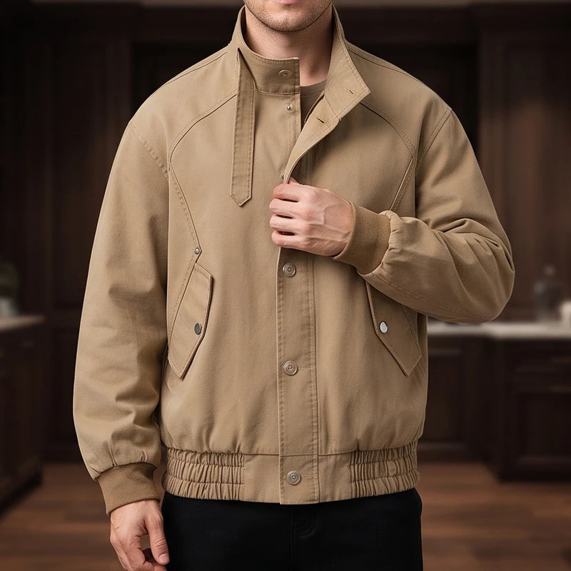 Man wearing a tan bomber jacket with a stand collar, snap buttons, side flap pockets, and elastic cuffs and hem.