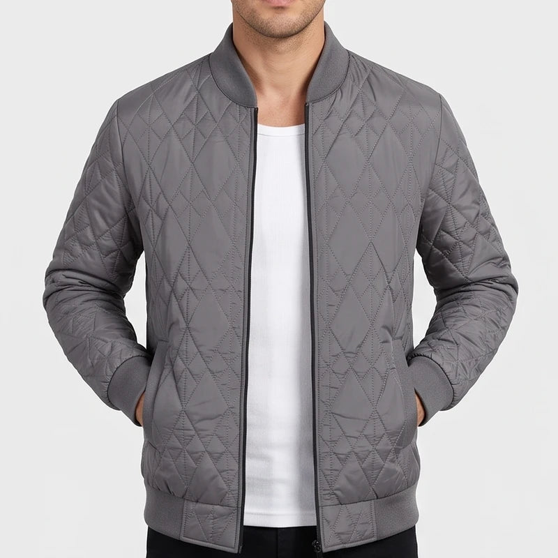 Man wearing a grey quilted bomber jacket with ribbed cuffs and collar, unzipped over a white t-shirt.