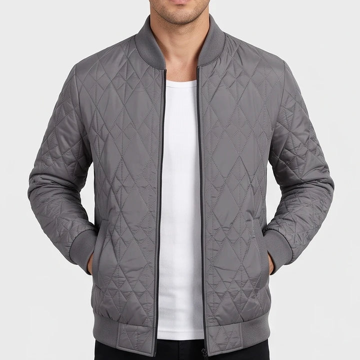 Man wearing a grey quilted bomber jacket with ribbed cuffs and collar, unzipped over a white t-shirt.