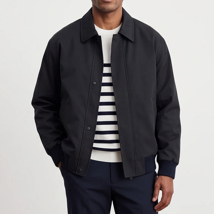 Man wearing a dark navy casual jacket with a collar, over a white and navy striped sweater and dark pants.