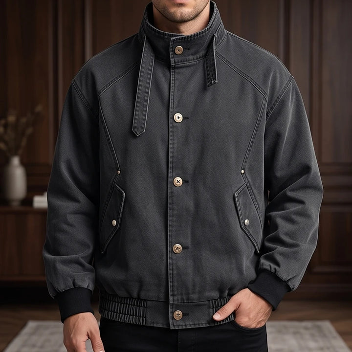 Man wearing a dark gray bomber jacket with a stand collar, brass buttons, and two front flap pockets.