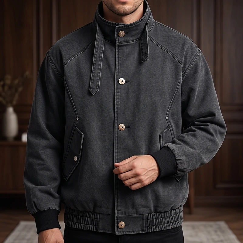Man wearing a dark gray washed bomber jacket with a high collar, tan buttons, and ribbed cuffs and hem.