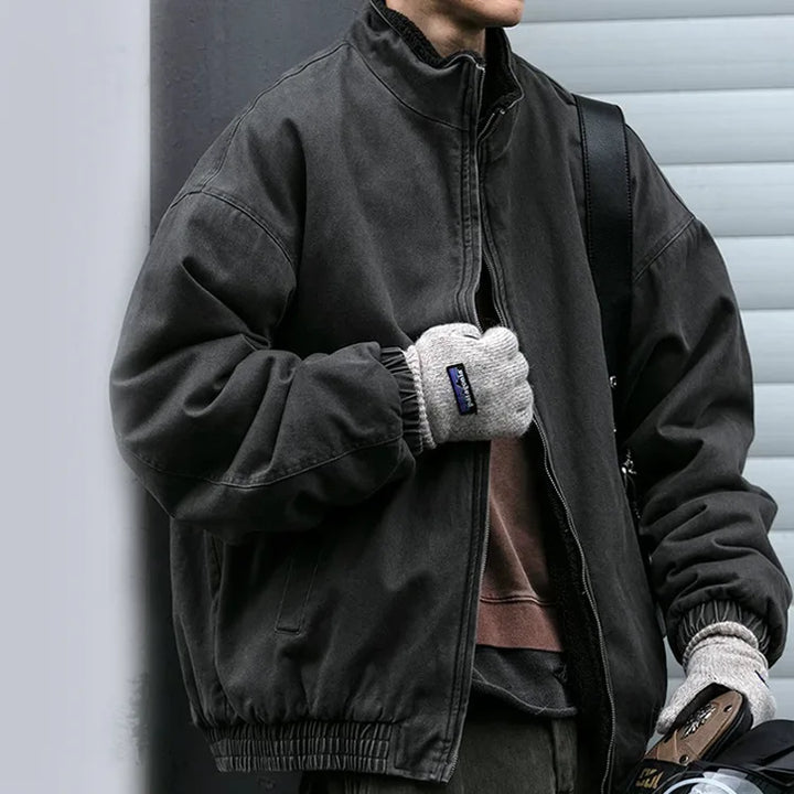Man wearing an oversized washed charcoal zip-up bomber jacket with elastic cuffs and hem, paired with grey knit gloves.