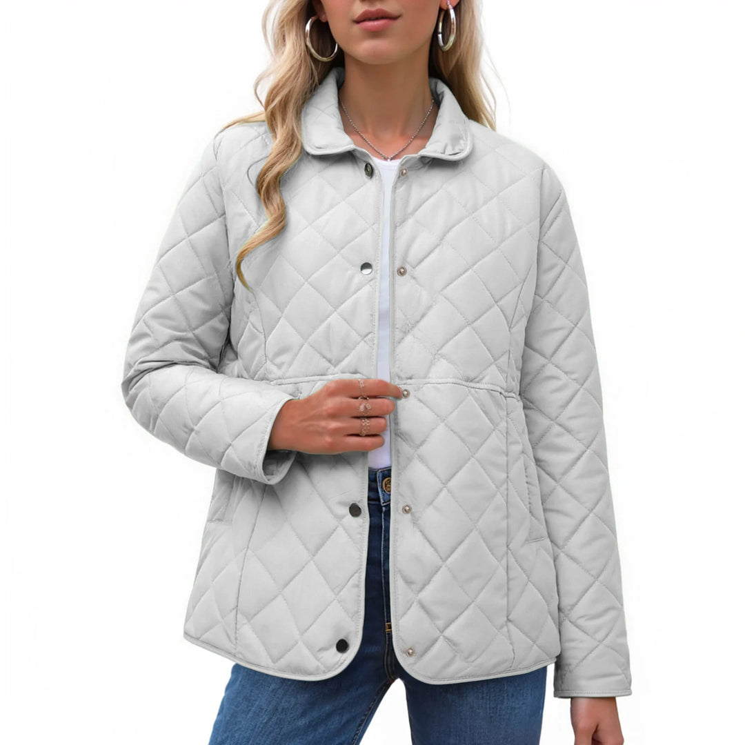 Woman wearing a light grey quilted jacket with a pointed collar, unbuttoned, over a white top and blue jeans.