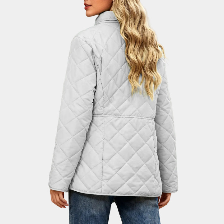 Woman wearing a light gray quilted jacket with a stand-up collar, paired with blue jeans, viewed from the back.