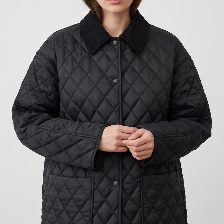 Woman wearing a black quilted jacket with a corduroy collar, hands clasped, against a plain white background.