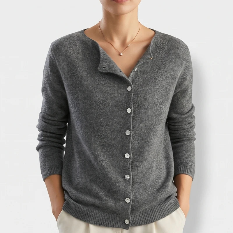 Woman wearing a dark gray knit cardigan with white buttons, V-neck, and ribbed trim, posing with hands in pockets.