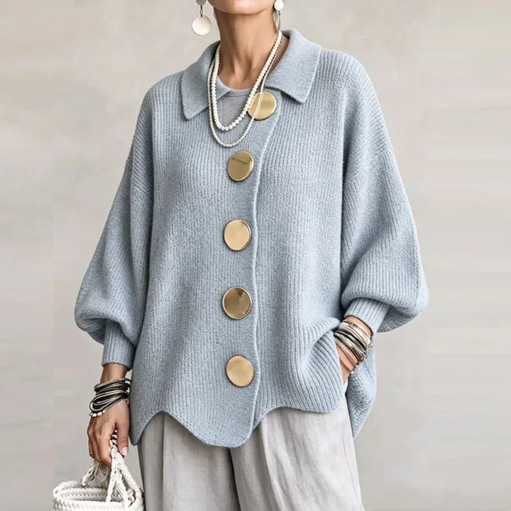 Woman wearing a light blue knit cardigan with an asymmetrical front, large gold circular buttons, and balloon sleeves.