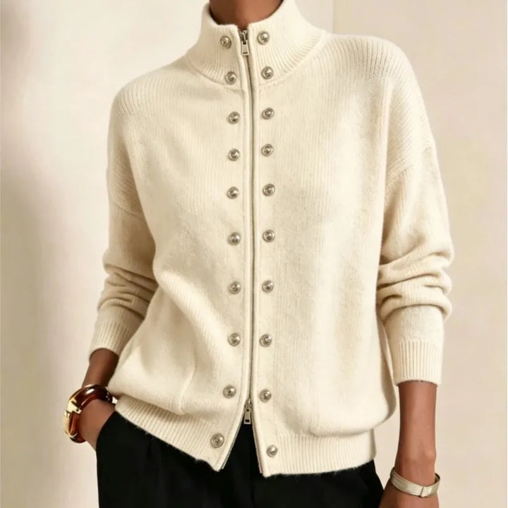Woman wearing an off-white knit jacket with a high collar, silver front zipper, and double rows of decorative silver buttons.