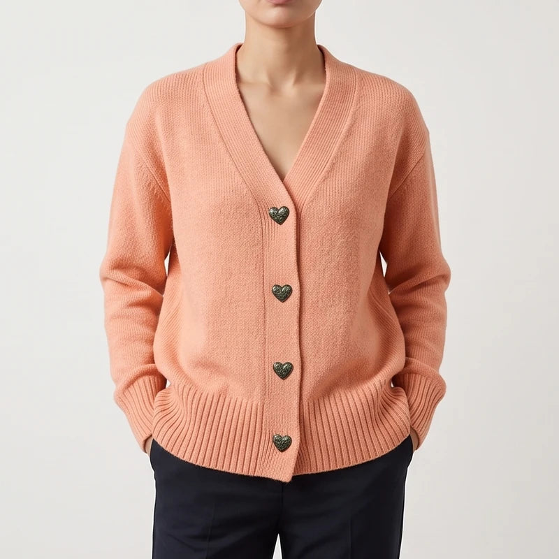 Woman wearing a peach knit cardigan with a V-neck, textured heart-shaped buttons, and ribbed cuffs and hem.