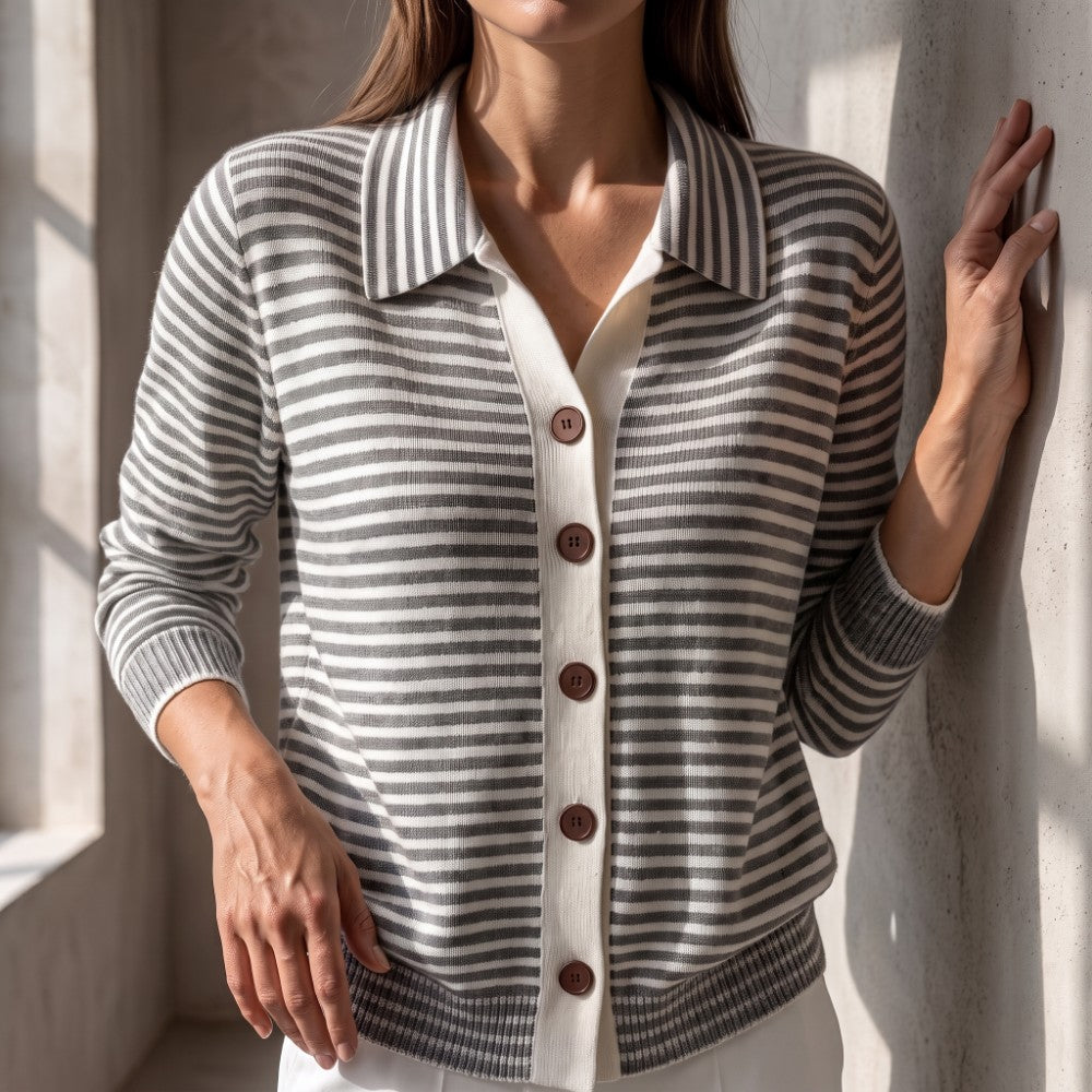 Woman wearing a grey and white striped knit cardigan with a collar, brown buttons, and ribbed cuffs, leaning on a wall.