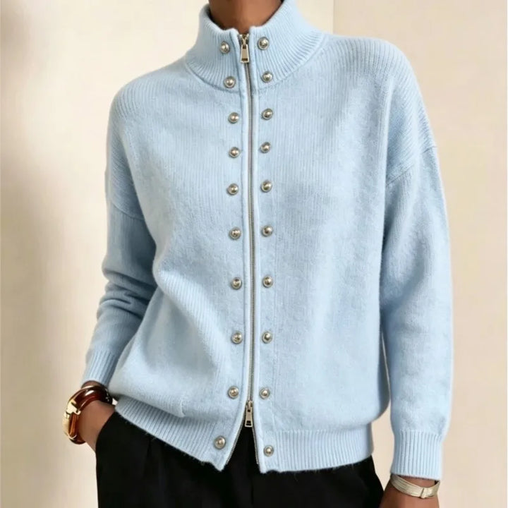 Woman wearing a light blue knit cardigan with a silver zipper and decorative silver studs on the front, hand in pocket.