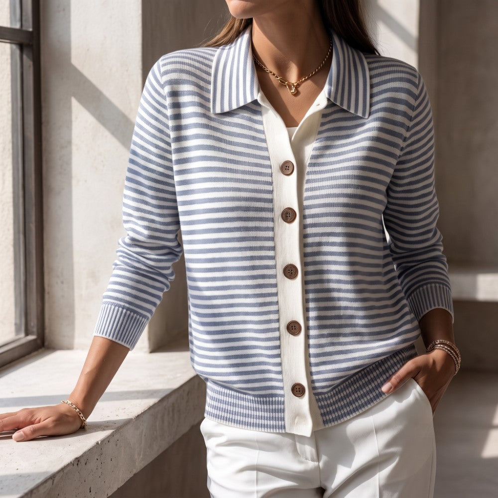 Woman wearing a blue and white striped knit cardigan with a collar, brown buttons, and white trim, standing by a window.