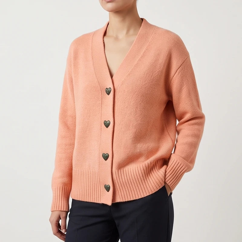 Woman wearing a peach knit cardigan with a V-neck, ribbed cuffs, and distinctive dark heart-shaped buttons.
