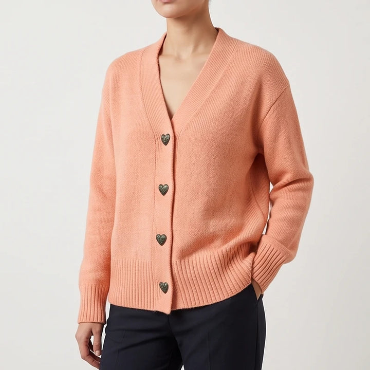 Woman wearing a peach knit cardigan with a V-neck, ribbed cuffs, and distinctive dark heart-shaped buttons.