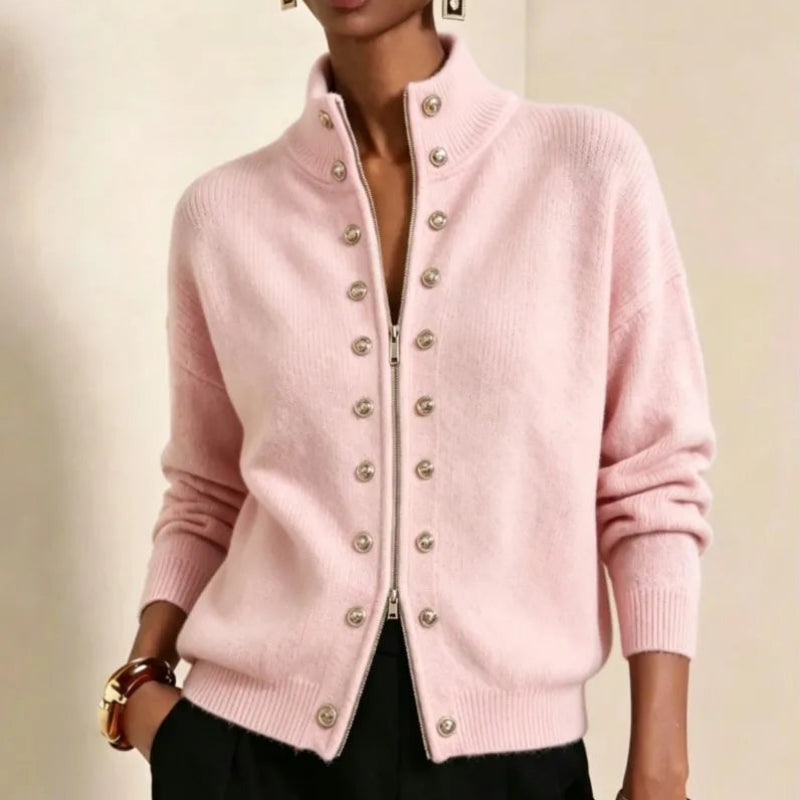 Woman wearing a light pink knit cardigan with a silver zipper and two rows of decorative silver buttons, set against a neutral background.