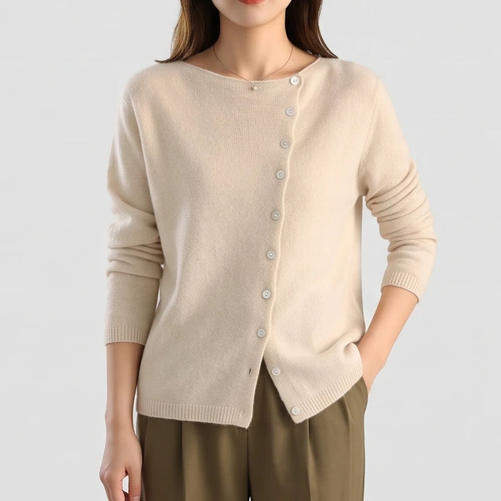 Woman wearing a beige knit cardigan with an asymmetric button placket and boat neckline, paired with olive pants.
