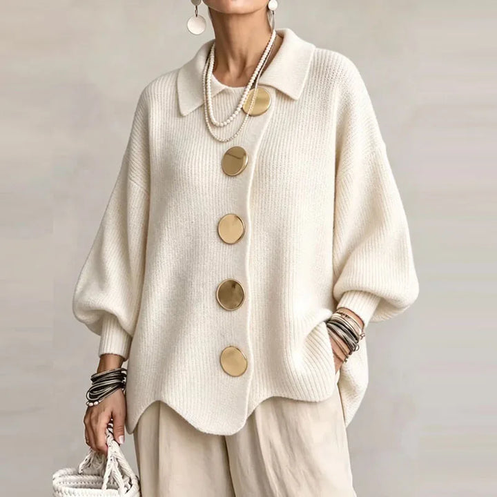 Woman wearing a cream knit cardigan with an oversized fit, large gold buttons, and a wavy hem.
