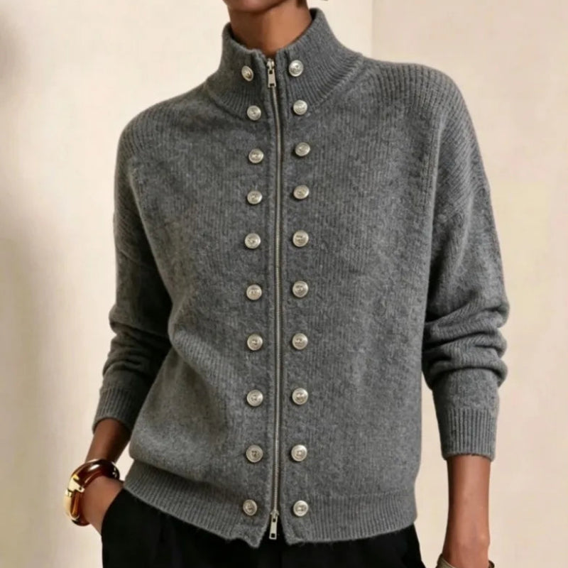 Close-up of a model wearing a gray knit zippered jacket with a high collar and two rows of decorative silver buttons.