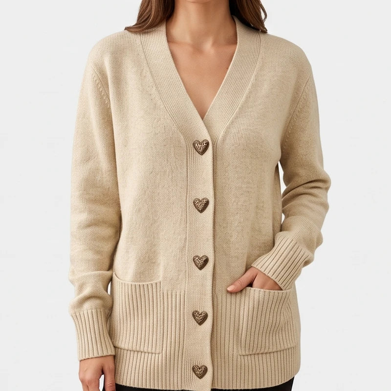 Woman wearing a beige knit cardigan with leopard print heart buttons, ribbed cuffs, and patch pockets, one hand in a pocket.