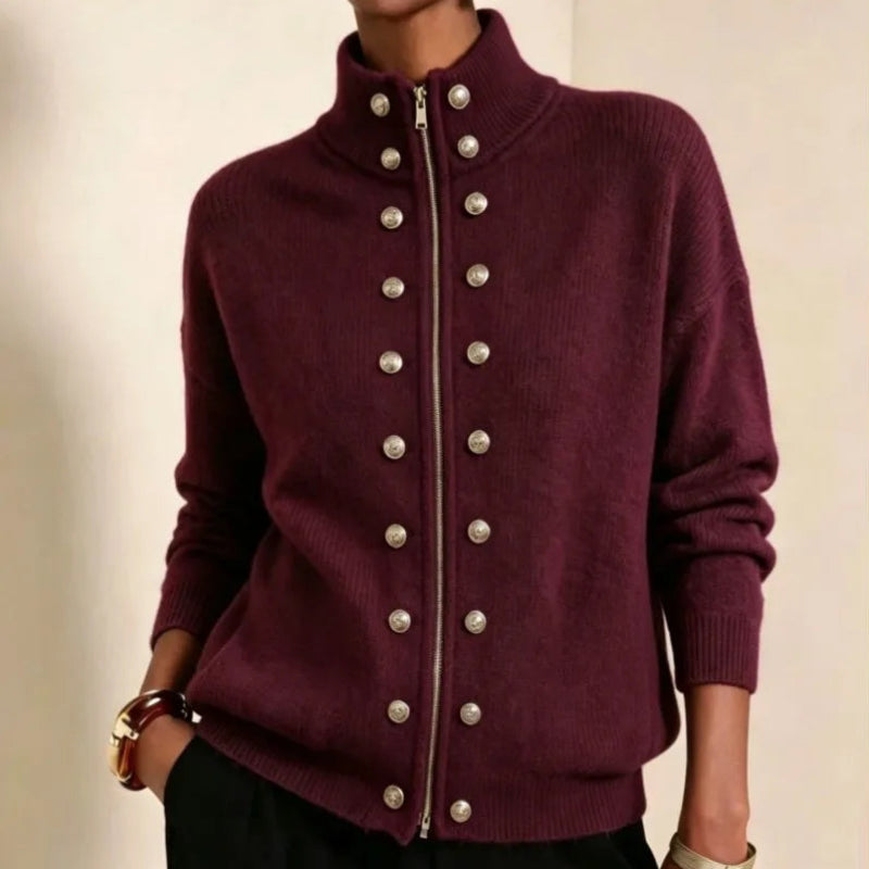 Woman wearing a fitted burgundy knit cardigan with a high collar, silver zipper, and two rows of decorative buttons.