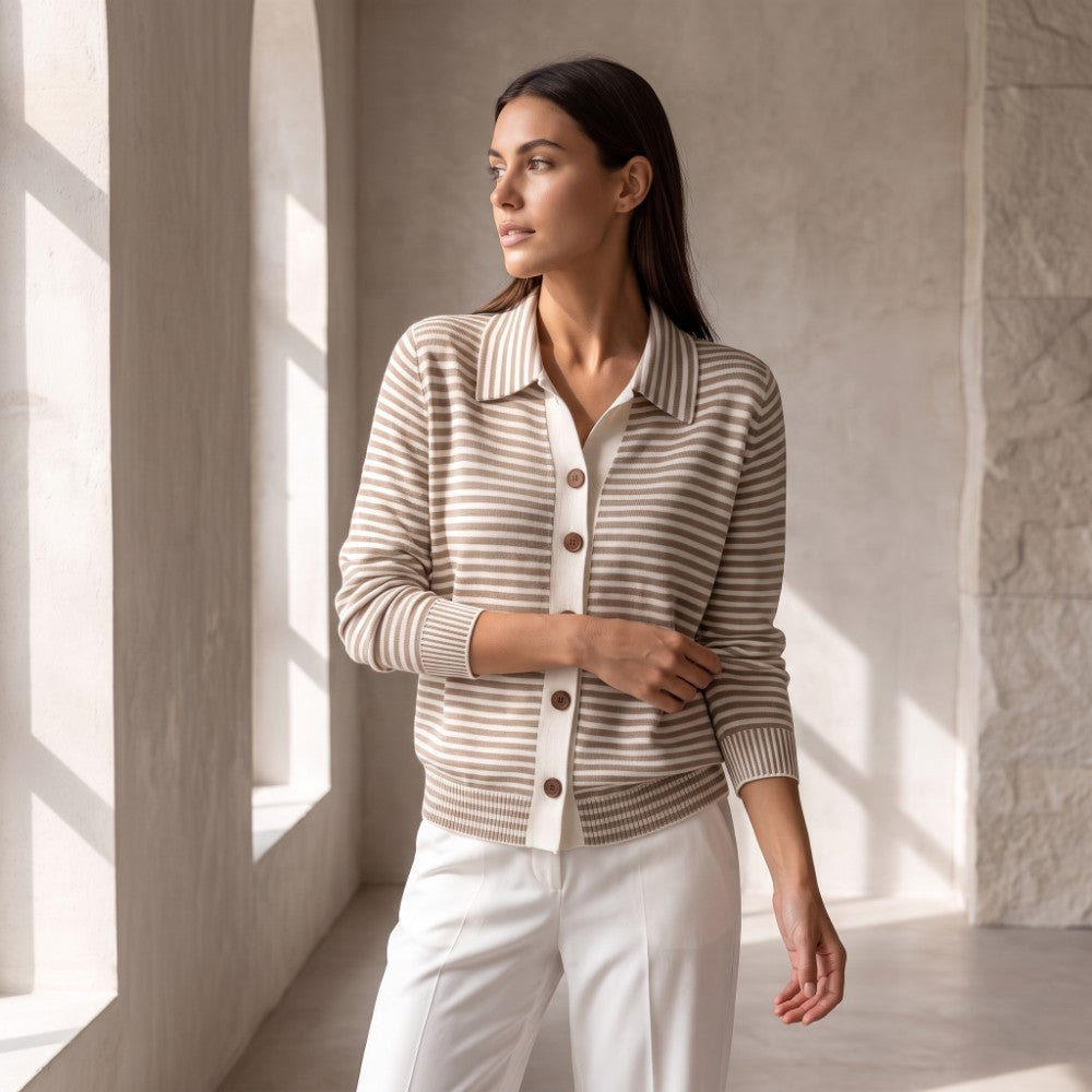 Woman looking left, wearing a collared, short beige and white striped knit top with brown buttons and white trousers.