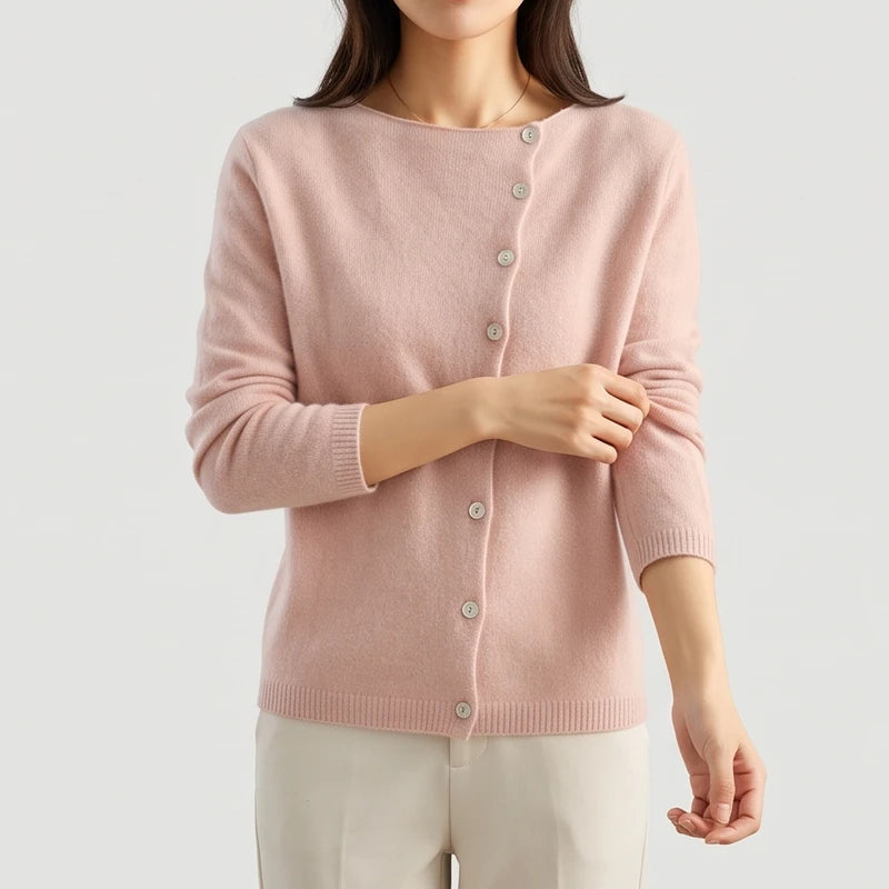 Woman wearing a soft pink knit cardigan with a boat neck and off-center light buttons, pulling up her sleeve.