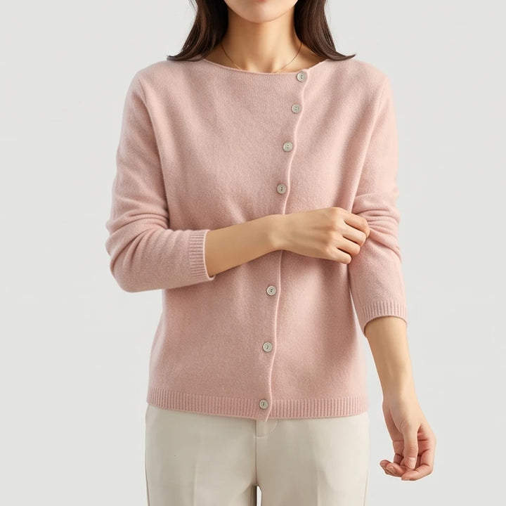 Woman wearing a soft pink knit cardigan with a boat neck and off-center light buttons, pulling up her sleeve.