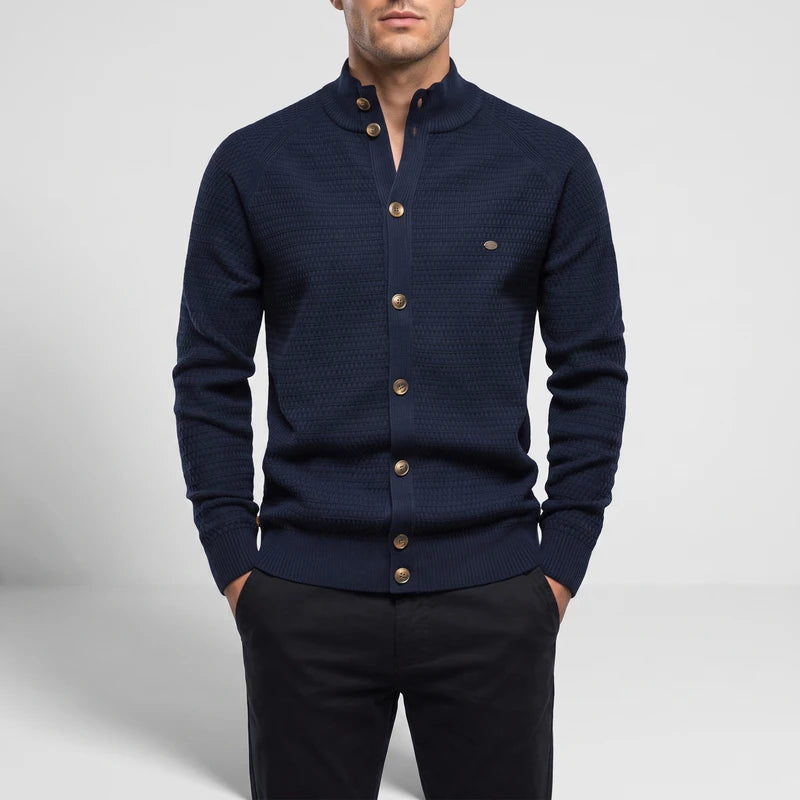 Man wearing a dark navy blue knit cardigan with a stand-up collar, gold buttons, and black pants.