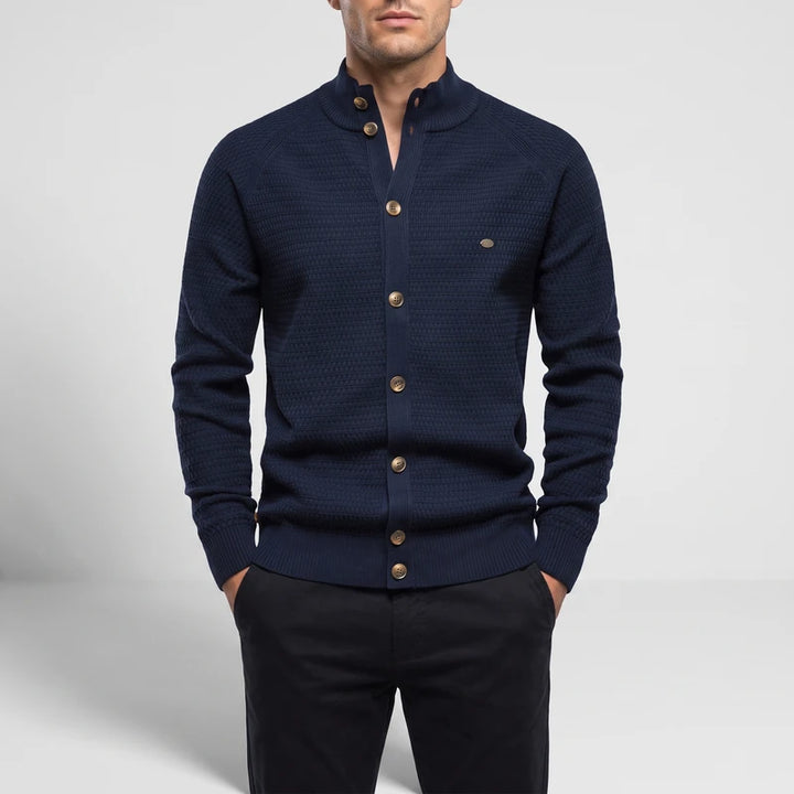 Man wearing a dark navy blue knit cardigan with a stand-up collar, gold buttons, and black pants.