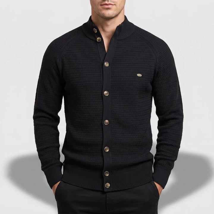 Man wearing a black knit cardigan with a textured waffle pattern and bronze buttons on a stand-up collar.