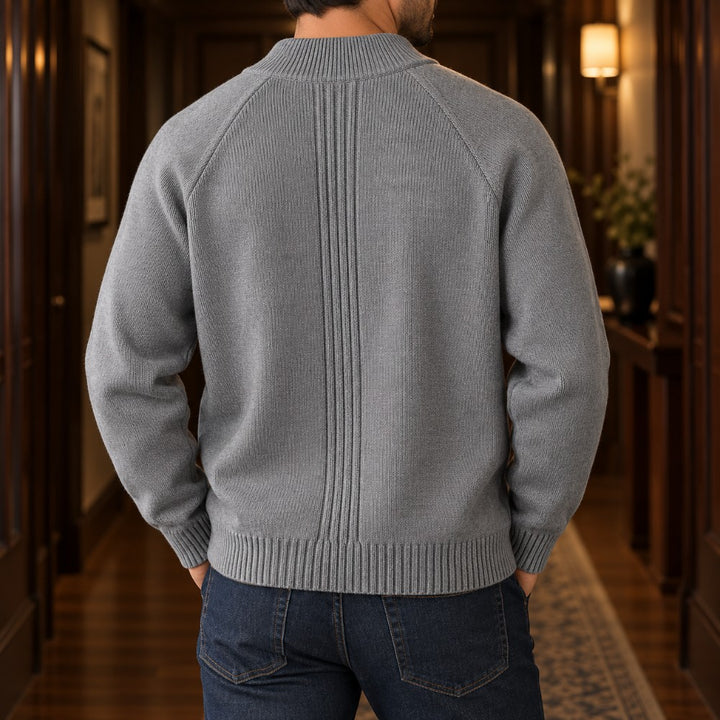 Man wearing a grey knit cardigan with a ribbed mock neck, vertical ribbed back panel, and dark blue jeans.