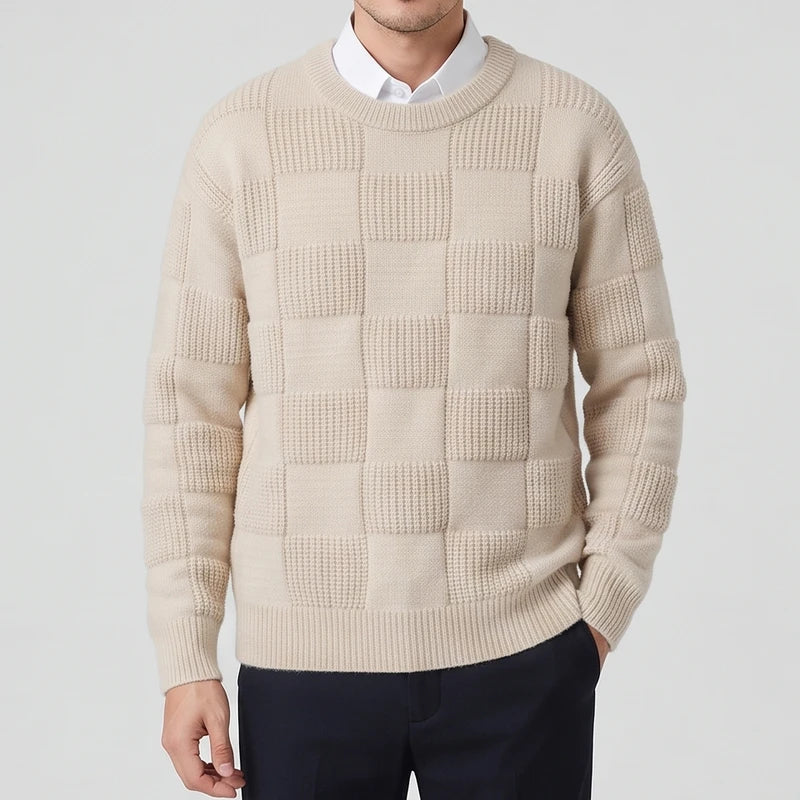 Man wearing a beige knit crew neck sweater with a checkerboard texture pattern, over a white collared shirt.