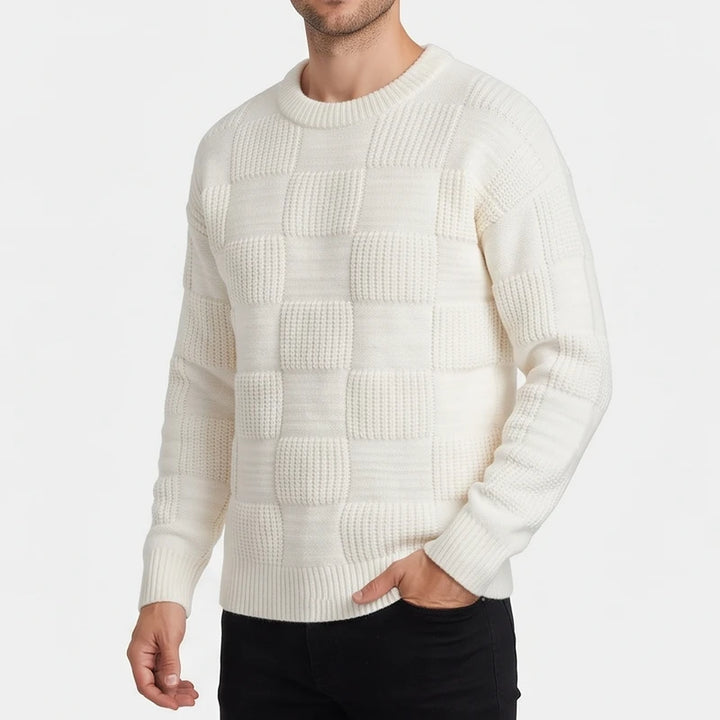 Man wearing a cream knit sweater featuring a checkerboard pattern of ribbed and smooth textured squares.