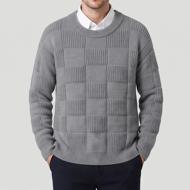Man wearing a grey knit sweater with an alternating checkerboard texture pattern over a white collared shirt.