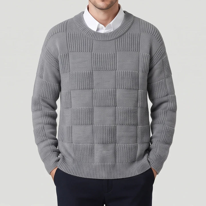 Man wearing a grey knit sweater with an alternating checkerboard texture pattern over a white collared shirt.