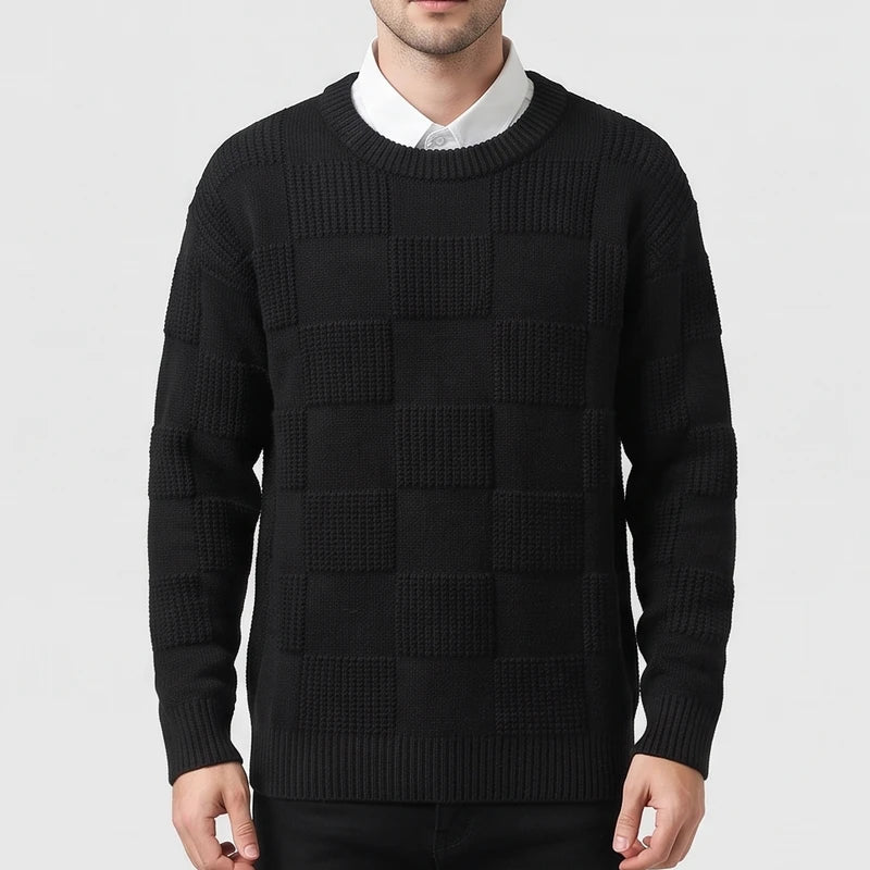 Man wearing a black checkerboard textured knit crew neck sweater over a white collared shirt.
