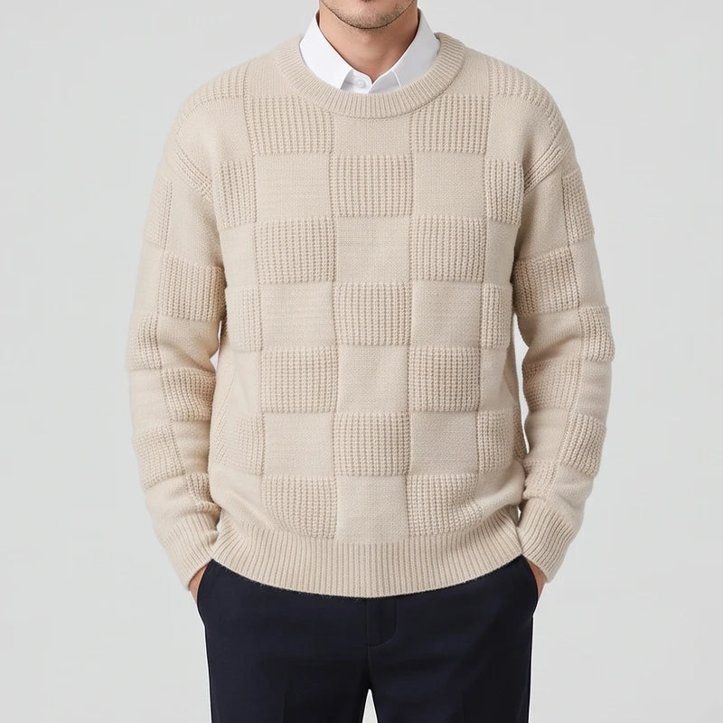 Man wearing a cream knit crew neck sweater with a checkerboard textured pattern over a white collared shirt.