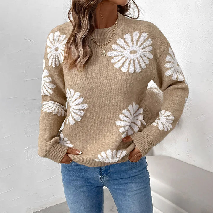 Woman wearing a loose-fitting beige knit sweater with large white daisy patterns, paired with blue jeans.