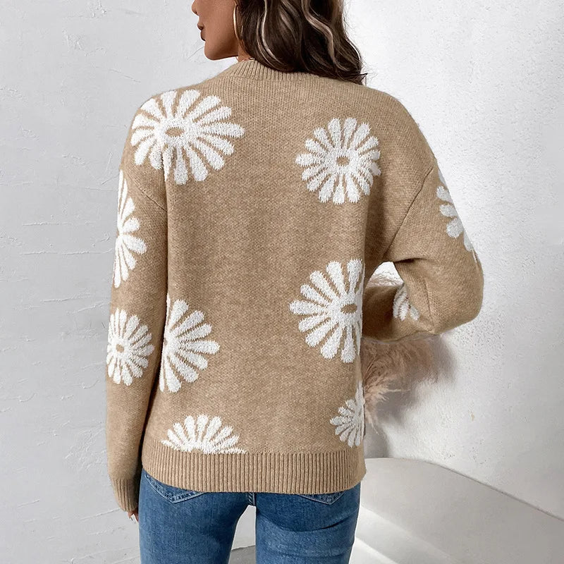 Woman wearing a relaxed-fit, light brown knit sweater with white daisy patterns, paired with blue jeans.