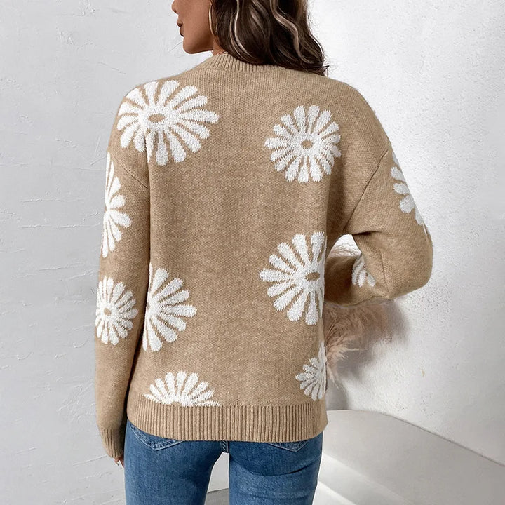 Woman wearing a relaxed-fit, light brown knit sweater with white daisy patterns, paired with blue jeans.