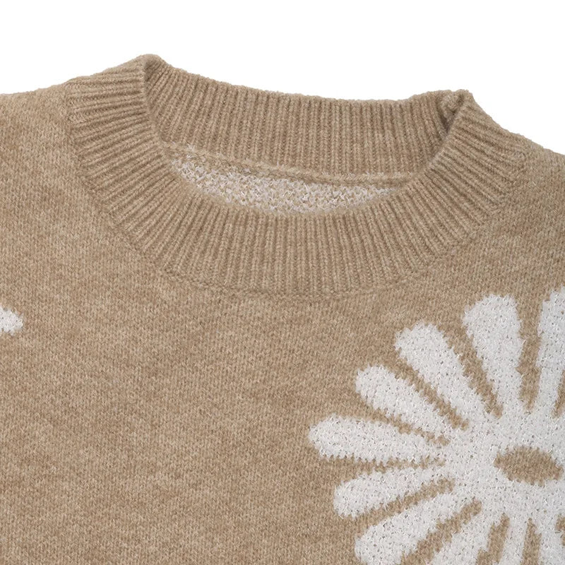 Close-up of a beige knitted sweater with a ribbed neckline and white daisy floral patterns.