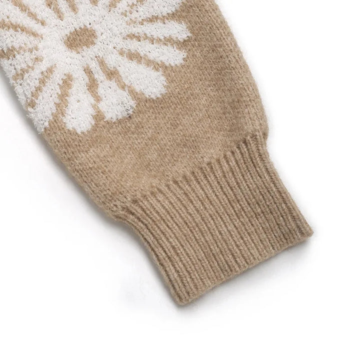 Close-up of a tan knit sweater sleeve with a white daisy pattern and a ribbed cuff on a white background.